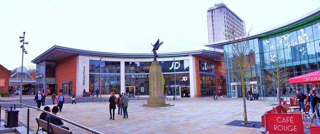 Woking town centre showing the Peacocks shopping centre, the Victoria Square war memorial statue, and shoppers crossing the pedestrianised square